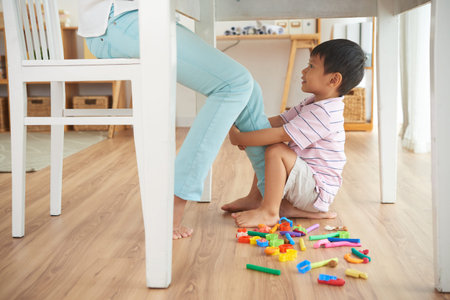 Cheerful Vietnamese boy playing with leg of his mom when she is workingの写真素材