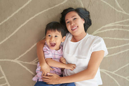 Happy hugging mother and son lying on the floorの写真素材