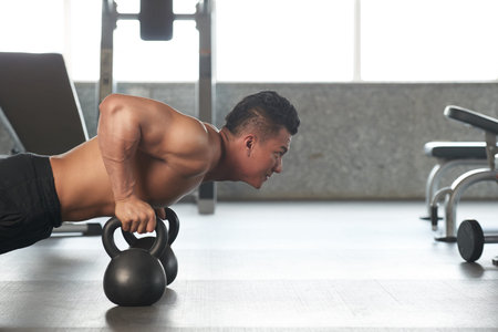 Sportsman using kettle bells when doing push-ups