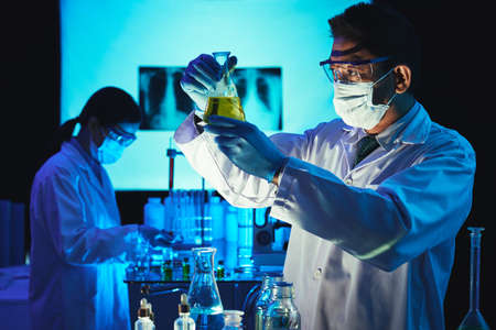 Vietnamese scientist looking at beaker with liquid in his handsの写真素材