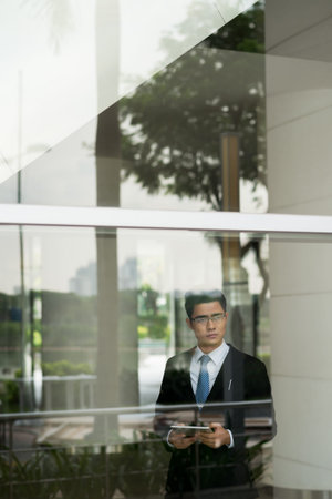 Vietnamese businessman with tablet computer standing inside office building