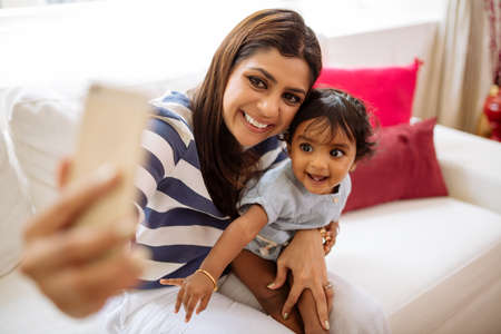 Happy Indian mother taking selfie with little daughterの写真素材