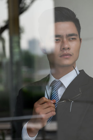 Pensive Vietnamese businessman with glasses in his hand looking in distanceの写真素材