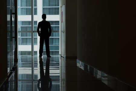 Rear view of business person looking at window of dark officeの写真素材