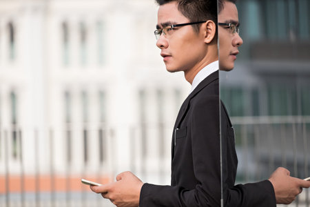 Entrepreneur with smartphone standing at mirror wallの写真素材