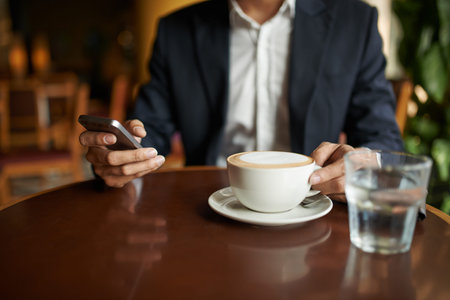 Hands of businessman drinking cappuccino and checking his phone