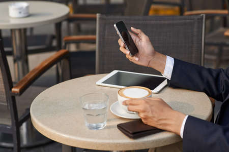 Hands of entrepreneur reading text message and drinking coffeeの写真素材
