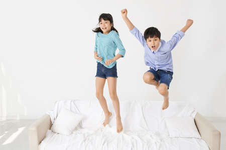 Joyful mixed-raced twins jumping on the bedの写真素材