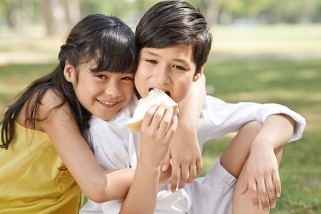Cheerful mixed-race girl hugging her brother who is eating sandwichの写真素材