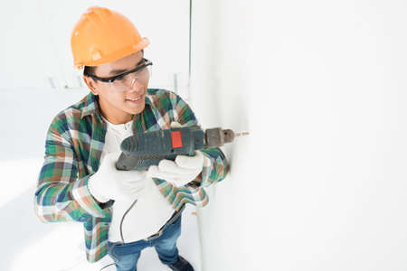 Man in hardhat making hole in wall with electric drillの写真素材