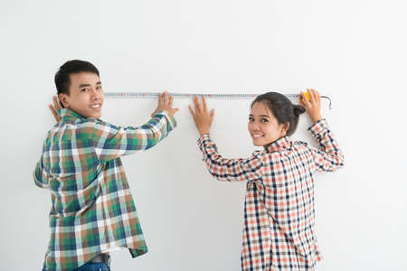 Young Vietnamese couple measuring wall with tapeの写真素材
