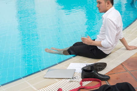 Entrepreneur having drink when sitting with legs in swimming poolの写真素材