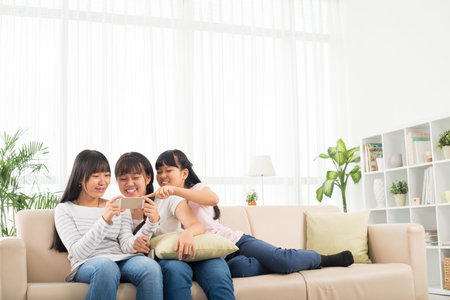 Teenage girls watching something on phone when resting at homeの写真素材