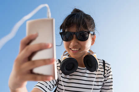 Face of preteen girl in sunglasses choosing music on her smartphoneの写真素材