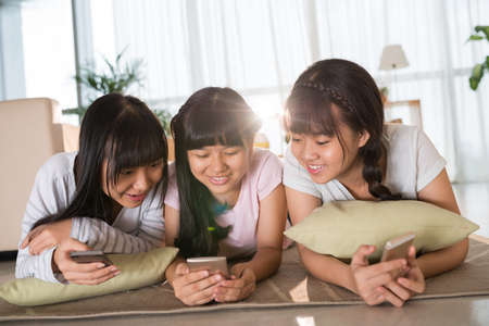 Girl lying on the floor and looking how their friend playing on smartphoneの写真素材