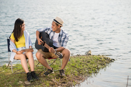 Man playing guitar for his girlfriend when resting at lakeの写真素材