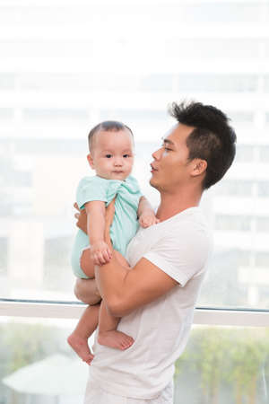 Vietnamese young man looking at adorable little baby in his handsの写真素材