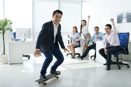 Business team cheering their chief on skateboardの写真素材