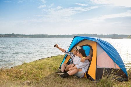 Couple sitting in tent and taking selfieの写真素材