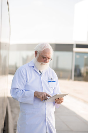 Mature general practitioner using digital tablet outdoors