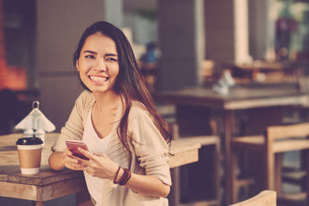 Portrait of beautiful Asian woman with mobile phone at cafe tableの写真素材