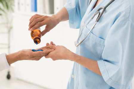 Doctor pouring pills into hand of female patientの写真素材