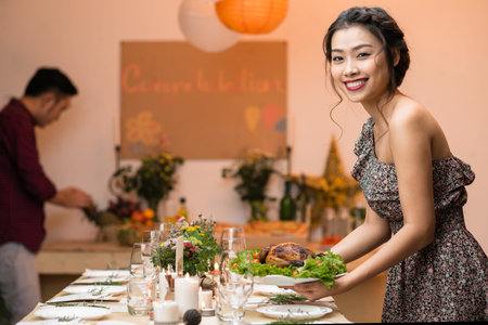 Attractive Vietnamese woman putting plate with fried chicken on dinner tableの写真素材