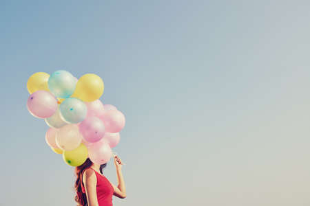 Girl with many colorful balloons against blue skyの写真素材