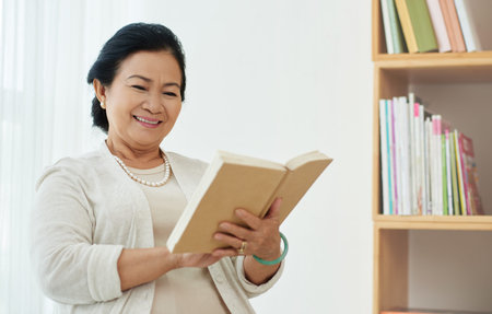 Aged Asian woman smiling when reading a bookの写真素材