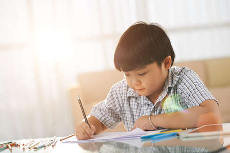 Vietnamese little boy sitting at table and drawing picturesの写真素材