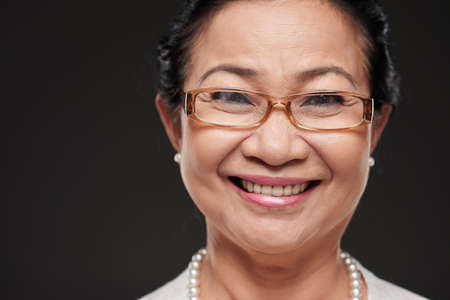 Face of Asian senior woman in glasses smiling at cameraの写真素材