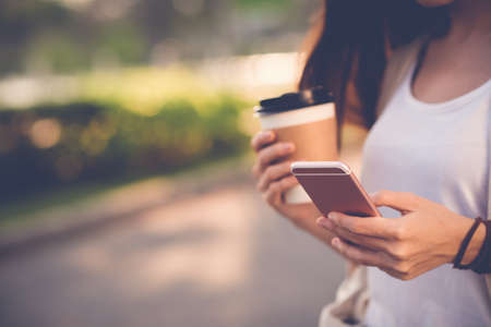 Close-up image of woman texting and drinking coffee outdoorsの写真素材