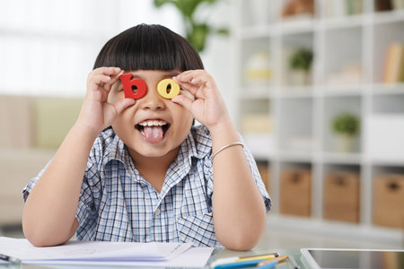 Boy holding plastic letter in front of his eyes and showing tongueの写真素材