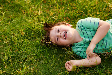 Laughing kid lying on green grass in the parkの写真素材