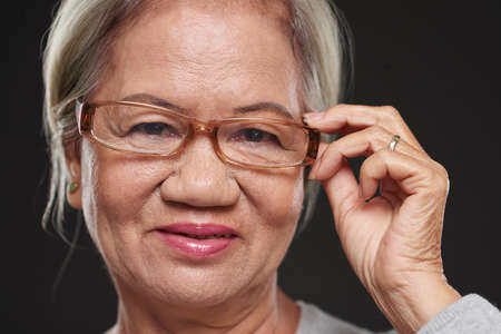 Face of aged Vietnamese woman adjusting her glassesの写真素材