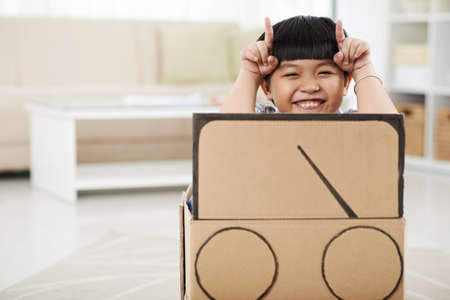 Cute boy making faces when sitting in cardboard carの写真素材