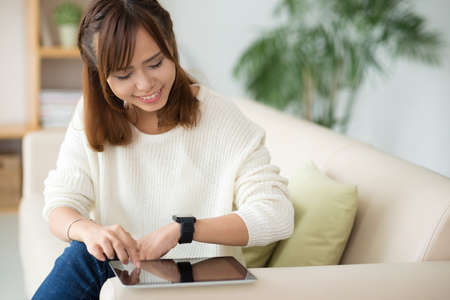 Smiling Asian woman synchronizing her smart watch and digital tabletの写真素材