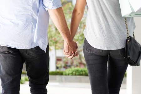 Rear view of couple holding hands when walking outdoorsの写真素材