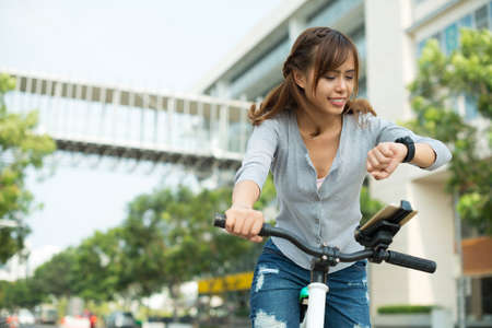 Pretty woman checking watch while cycling in the cityの写真素材