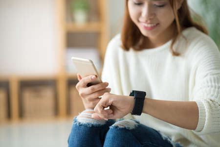 Young Asian woman synchronizing her smartphone and smart watchの写真素材