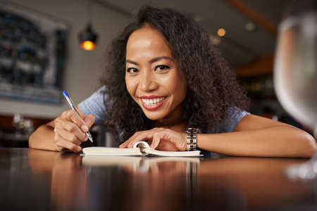 Portrait of cheerful woman in bar making notesの写真素材