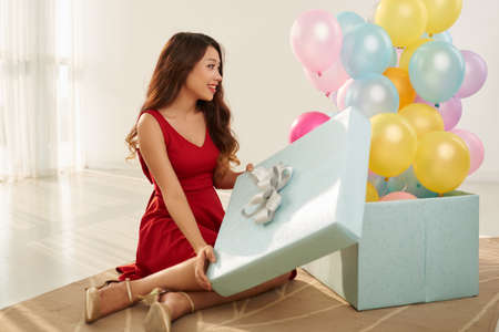 Cheerful beautiful woman opening gift box full of balloonsの写真素材