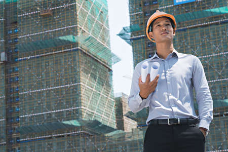 Portrait of young Asian engineer with rolled construction plansの写真素材