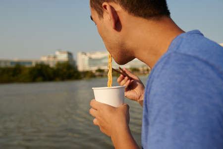 Man eating instant noodles and looking at the riverの写真素材