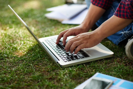 Close-up image of man typing on laptop when sitting on grassの写真素材