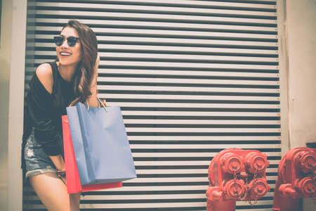 Pretty cheerful girl with shopping bags standing at the wallの写真素材
