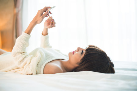 Beautiful young woman lying in bed and textingの写真素材