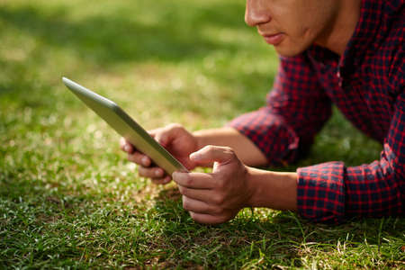 Man lying on grass and watching something on digital tabletの写真素材