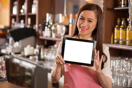 Smiling Vietnamese waitress showing digital tablet with white screenの写真素材