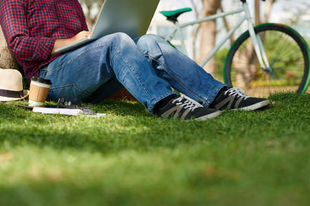 Cropped image of man sitting in park and working on laptopの写真素材